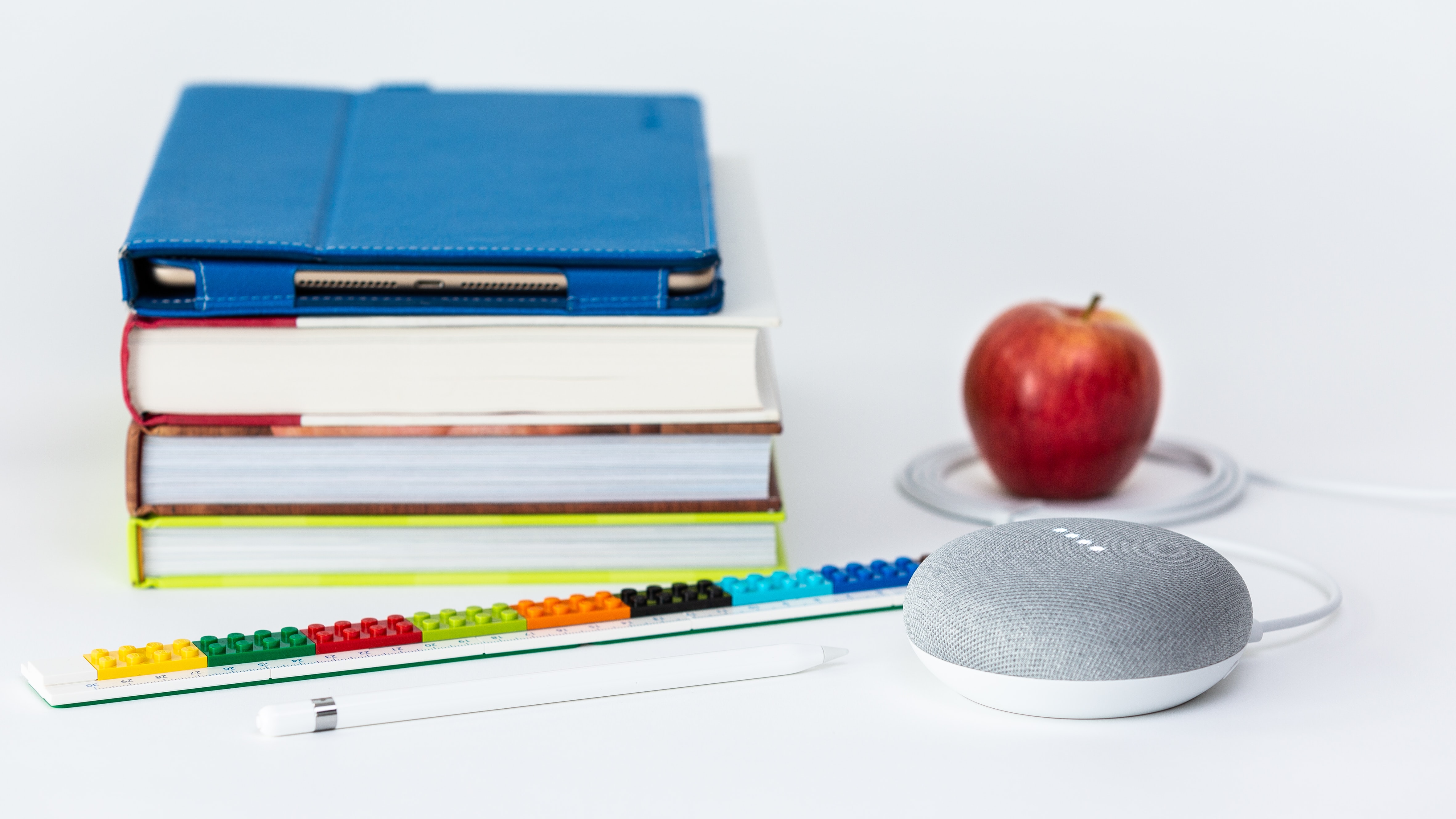 academic books stacked up with an apple and Legos and a speaker